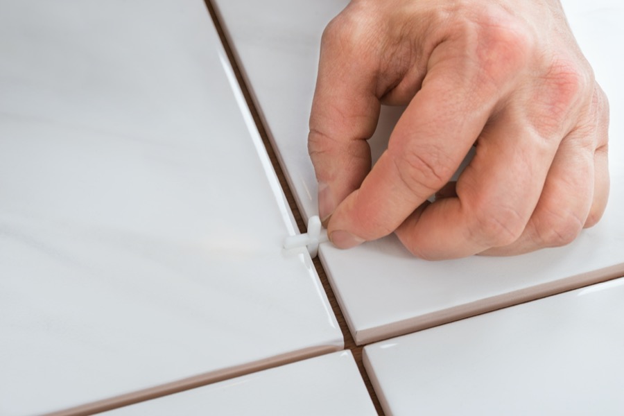 person's hand placing spacers between ceramic floor tiles